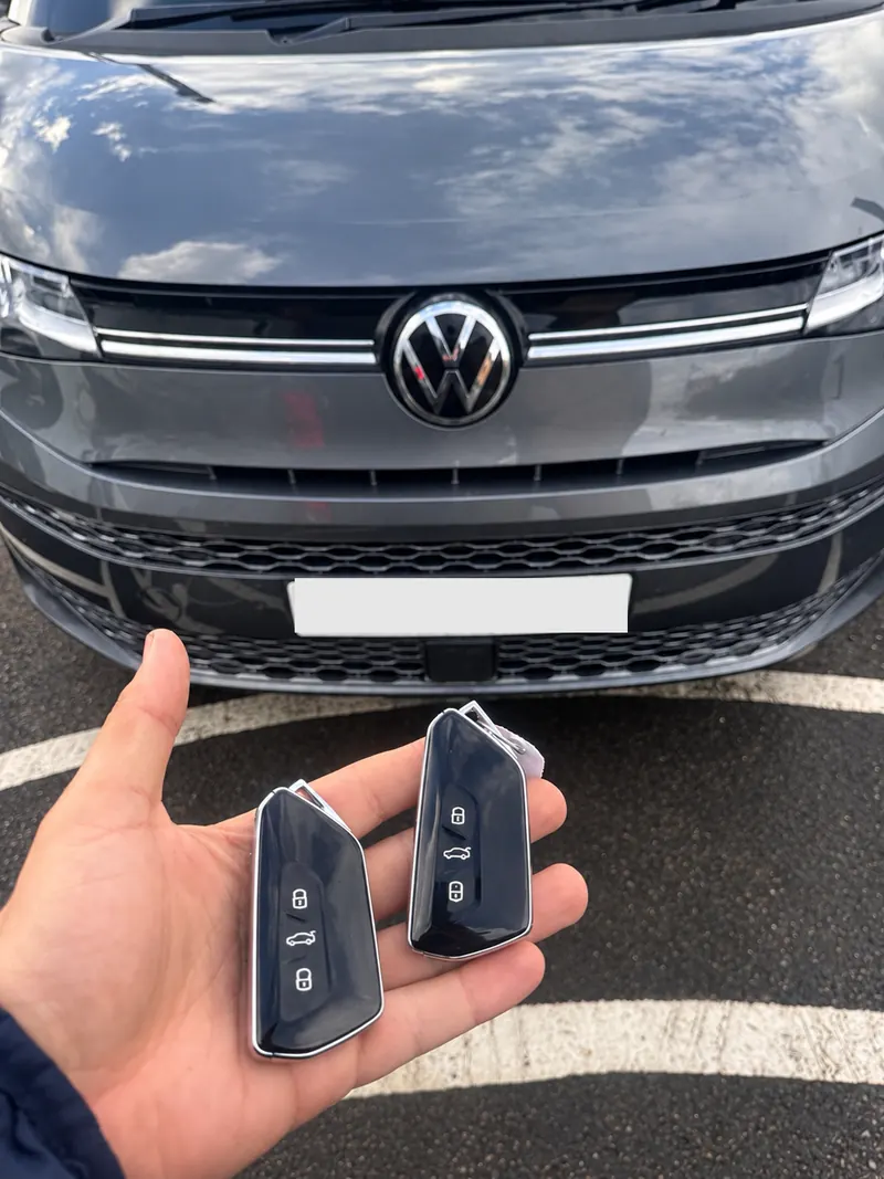 Grey Volkswagen van with two glossy black Volkswagen smart keys held in front of it, number plate obscured